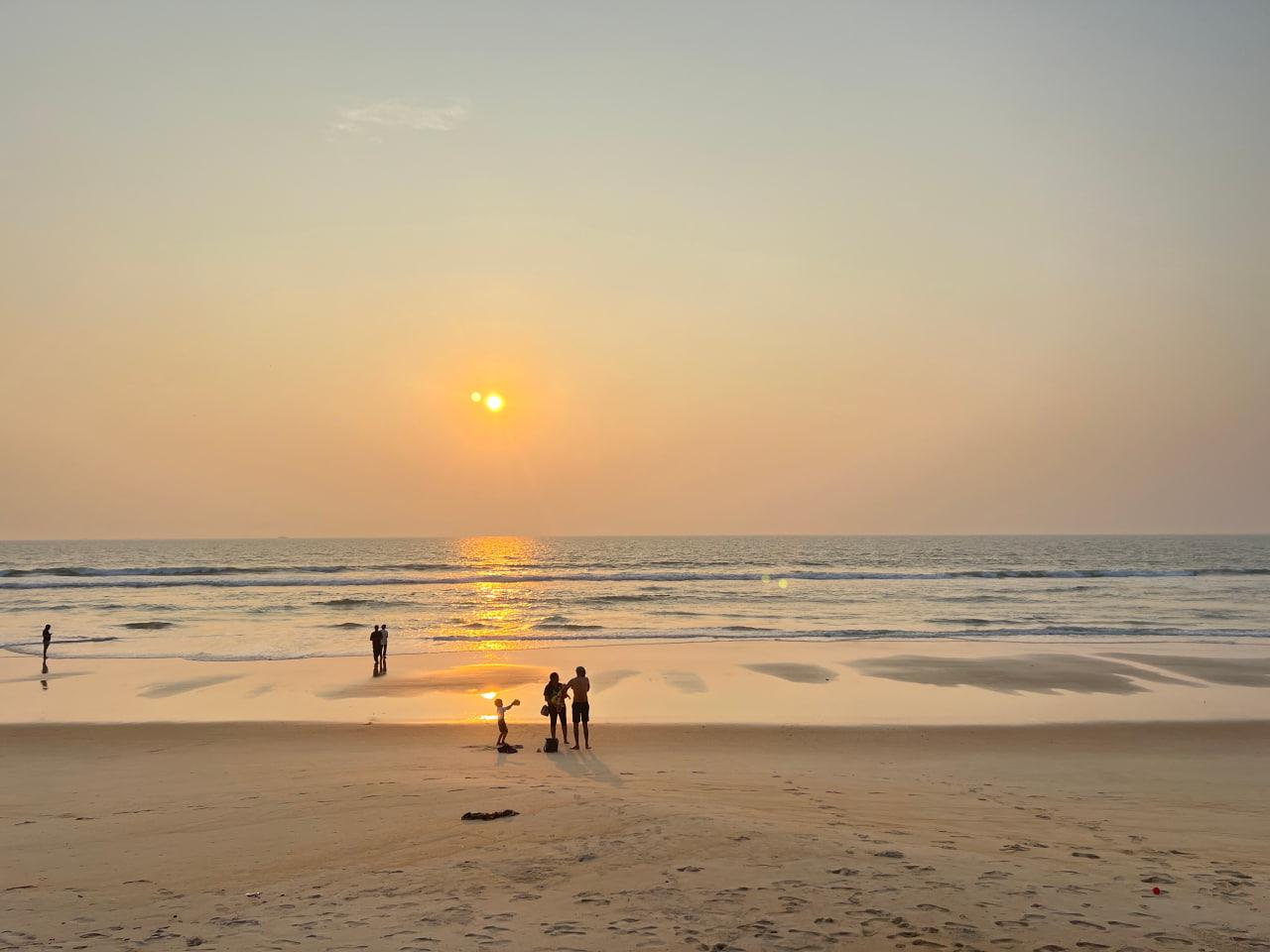 People enjoying the beach as the setting sun reflects across the water and sand