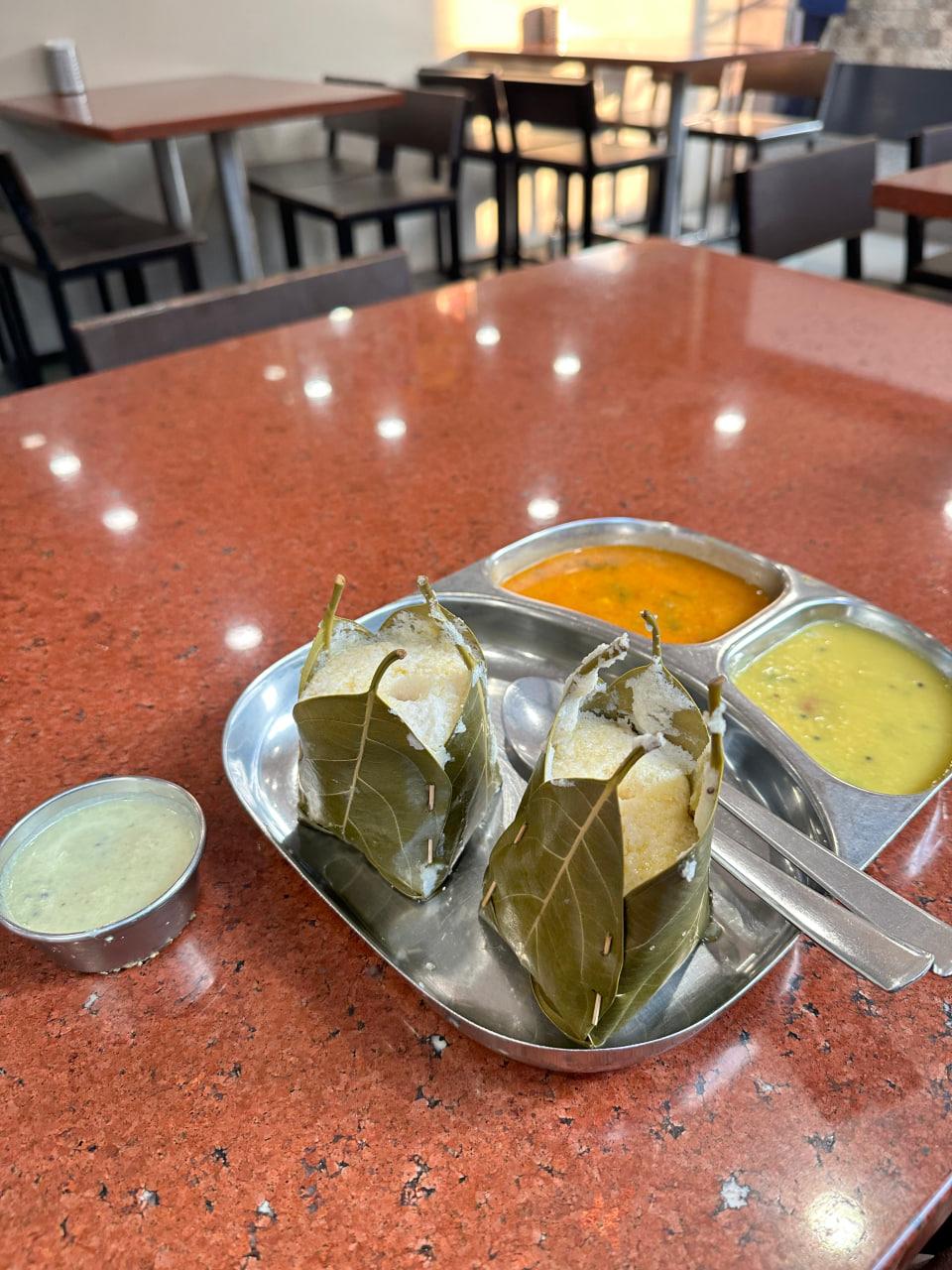 Leaf-wrapped idlis served with sambar and chutney on a steel plate